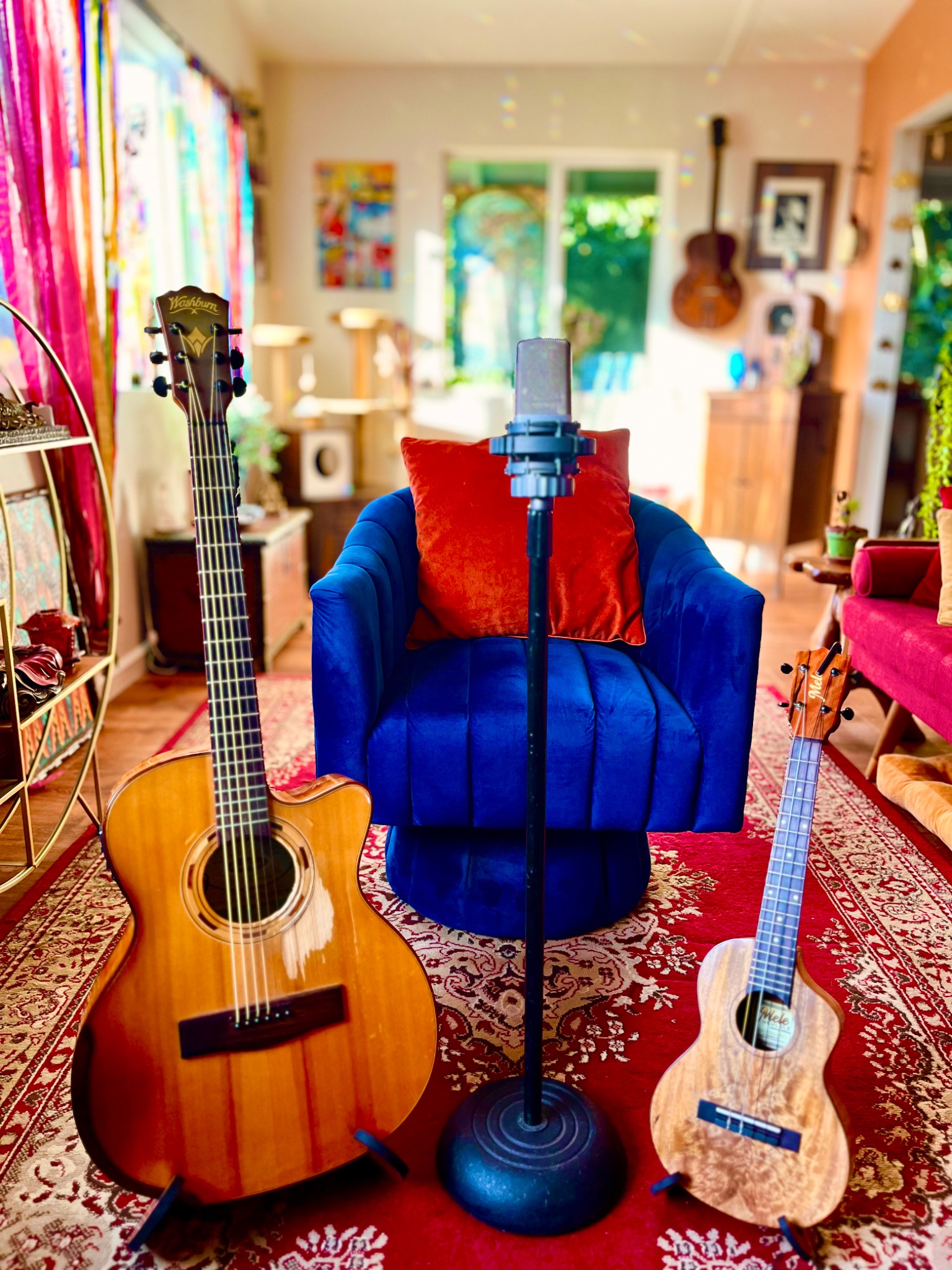 A microphone in front of a blue chair, with an acoustic guitar and ukulele in Music Medicine Studio